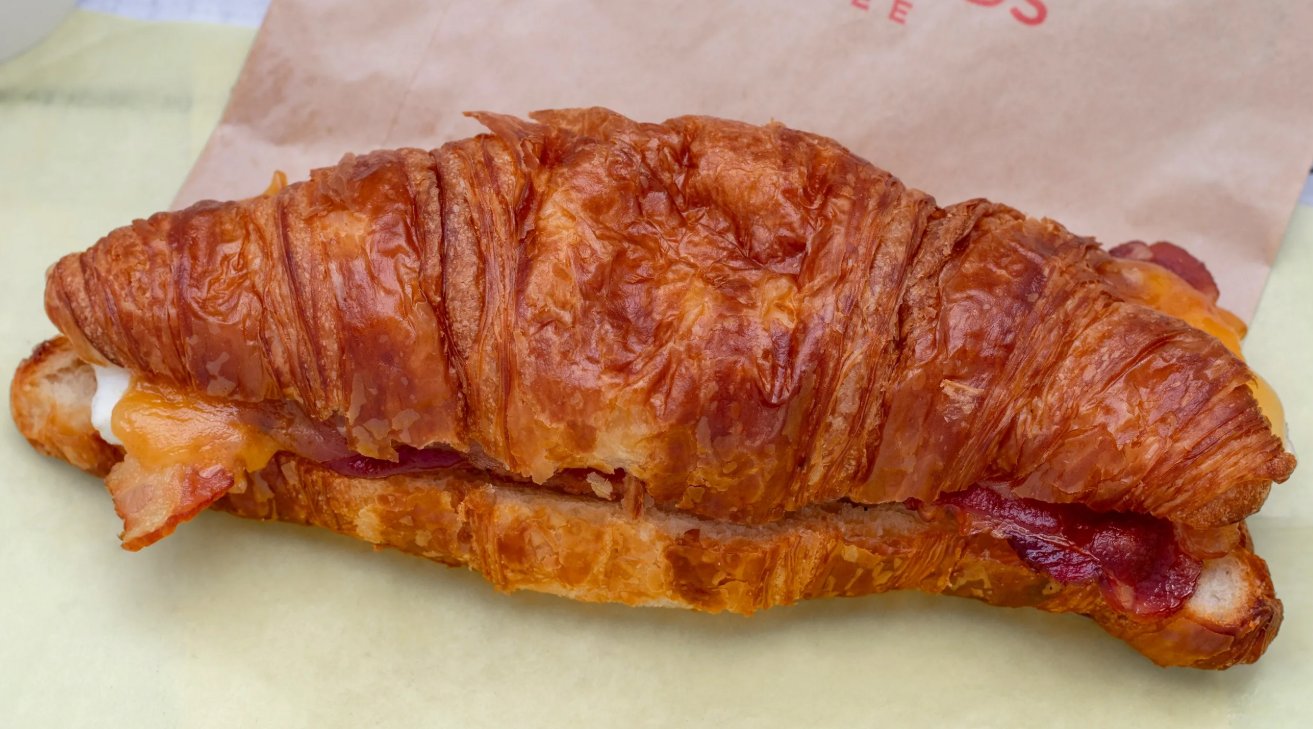 A golden bacon and cheddar croissant on a Riverwoods Coffee paper bag