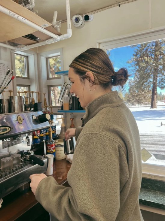 A Riverwoods Coffee barista pulling espresso shots inside the stand with a snowy Bend forest out the window